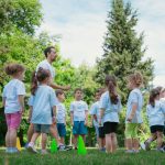 Group of children and teachers playing and learning in a sunny park setting.